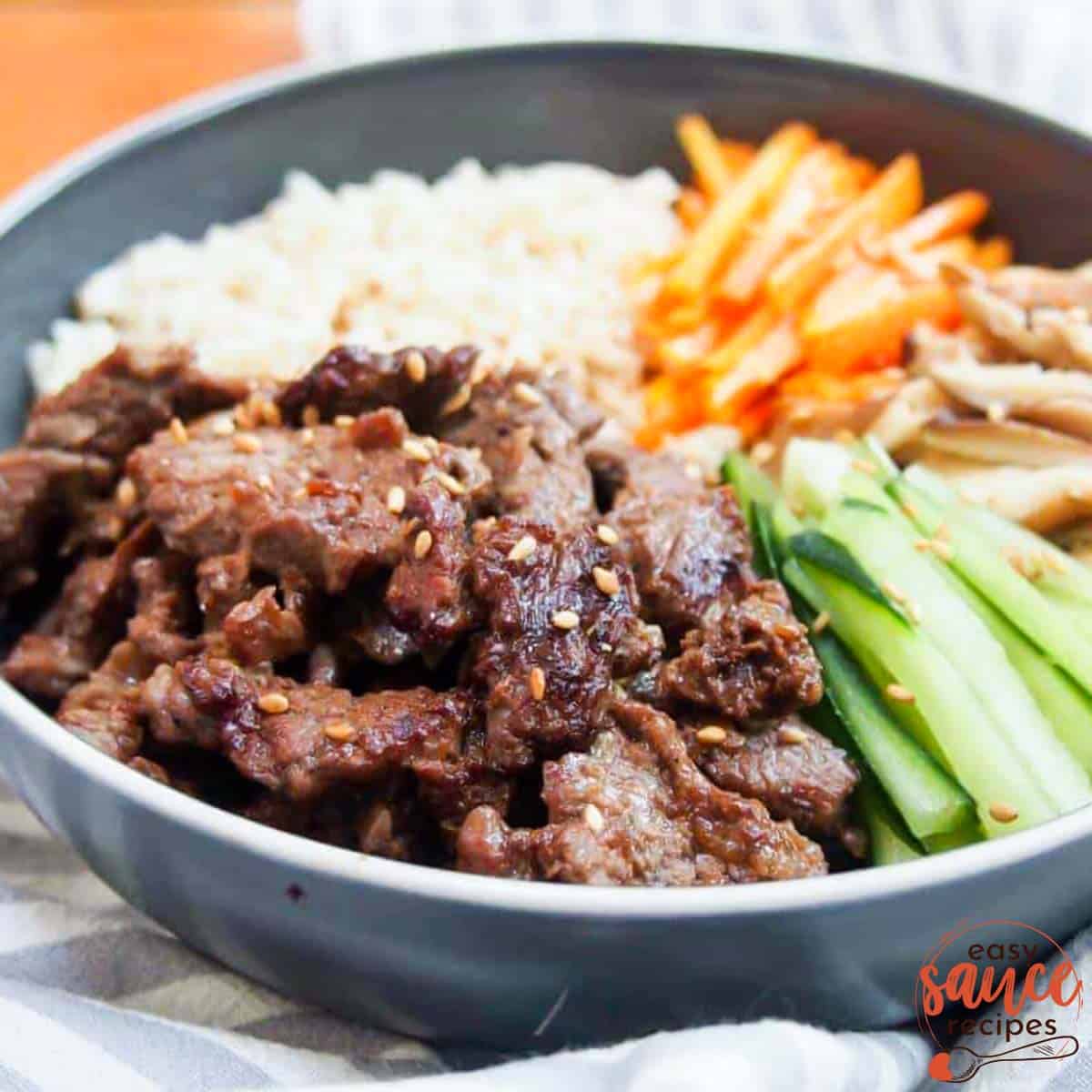 bulgogi marinated beef in a bowl with rice, mushrooms, carrots, and cucumbers, up close