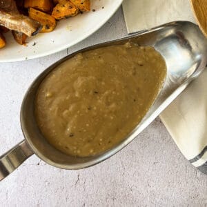 brown gravy inside a metal gravy boat with a white napkin