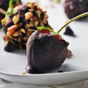 a chocolate ganache dipped strawberry next to another one with a nut coating