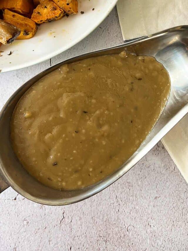 brown gravy inside a metal gravy boat with a white napkin
