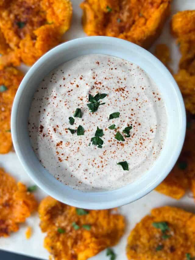a white dish full of dipping sauce surrounded by sweet potato bites on a white cutting board