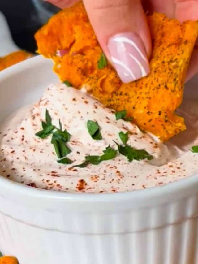 a sweet potato chip being dipped into a dish of dipping sauce