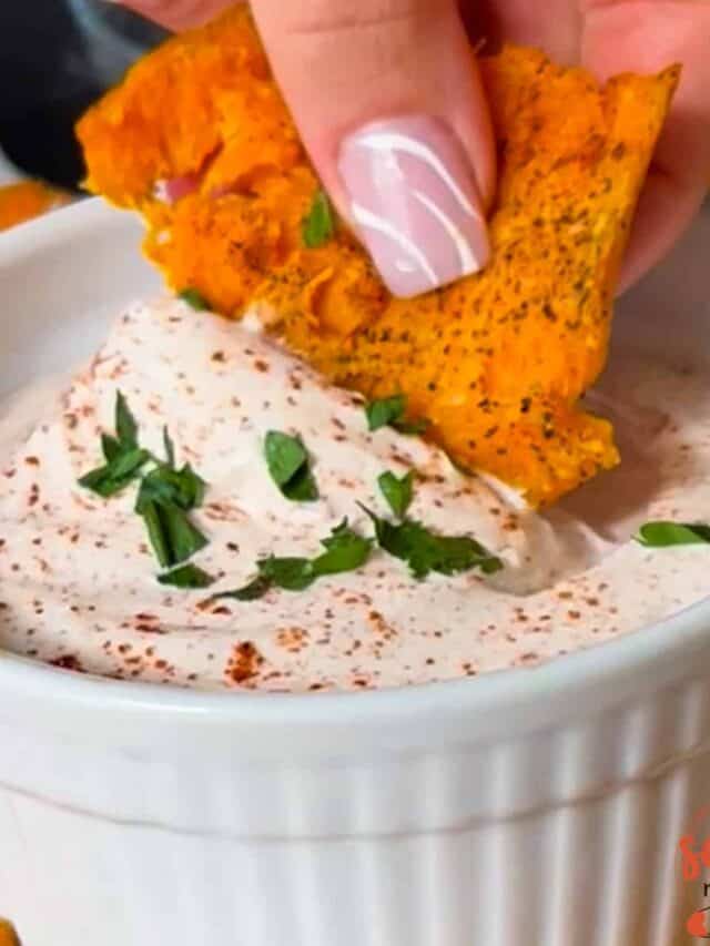 a sweet potato chip being dipped into a dish of dipping sauce