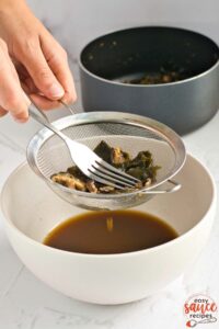 straining vegan fish sauce into a bowl with a fork and a strainer