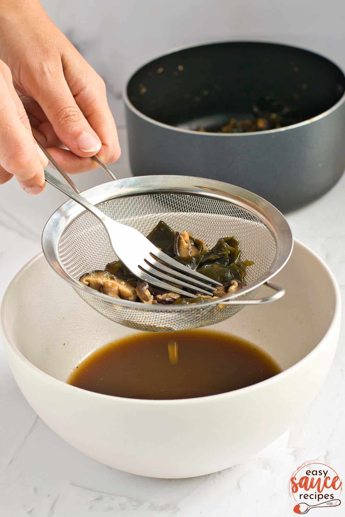 straining vegan fish sauce into a bowl with a fork and a strainer