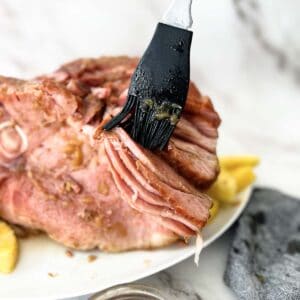 brushing pineapple glaze between slices of ham