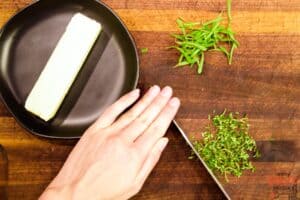 herbs being chopped on a cutting board next to softening butter