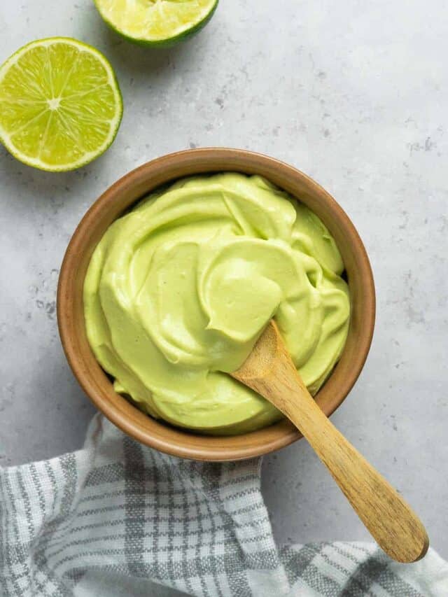 smoothly mixed avocado crema in a bowl with a wooden spoon