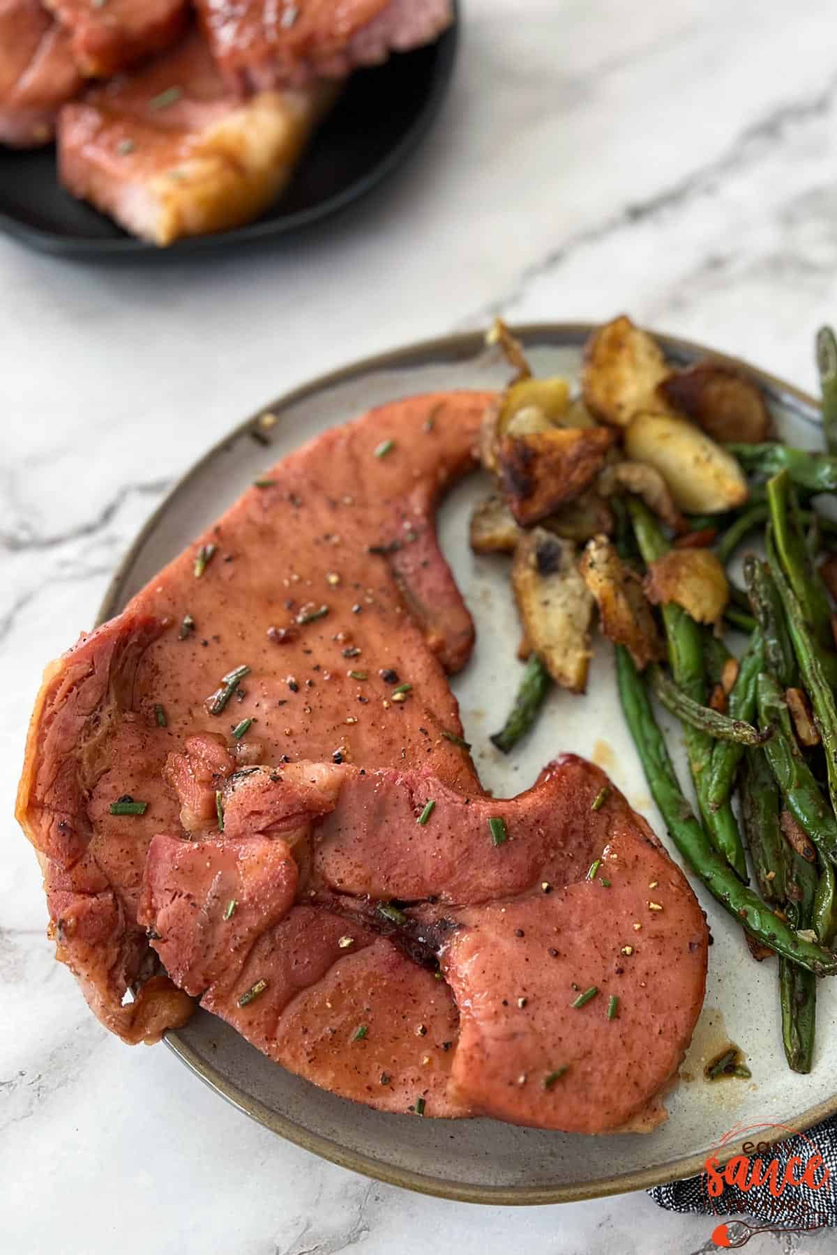 a dinner plate with ham steaks covered in ham steak glaze, green beans, and potatoes