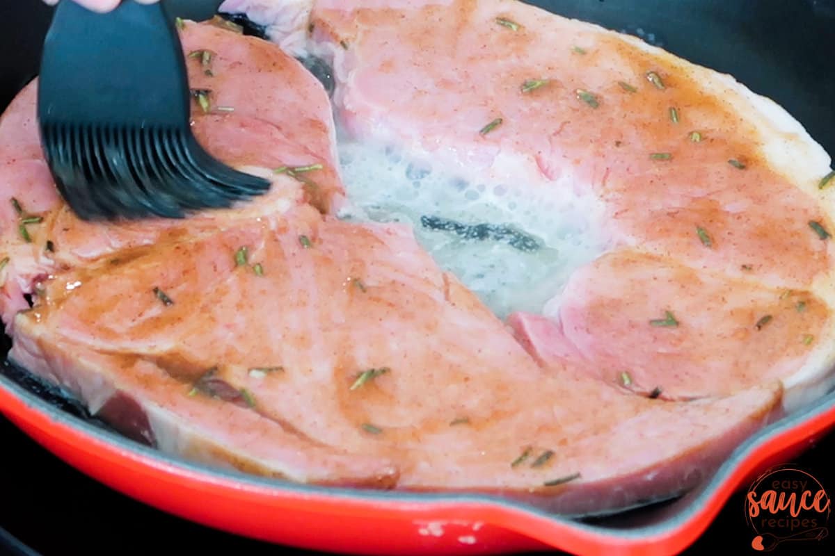 ham steaks in a pan being brushed with ham steak glaze