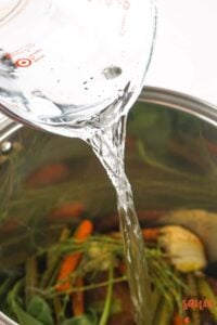 pouring water into stock pot over turkey stock ingredients