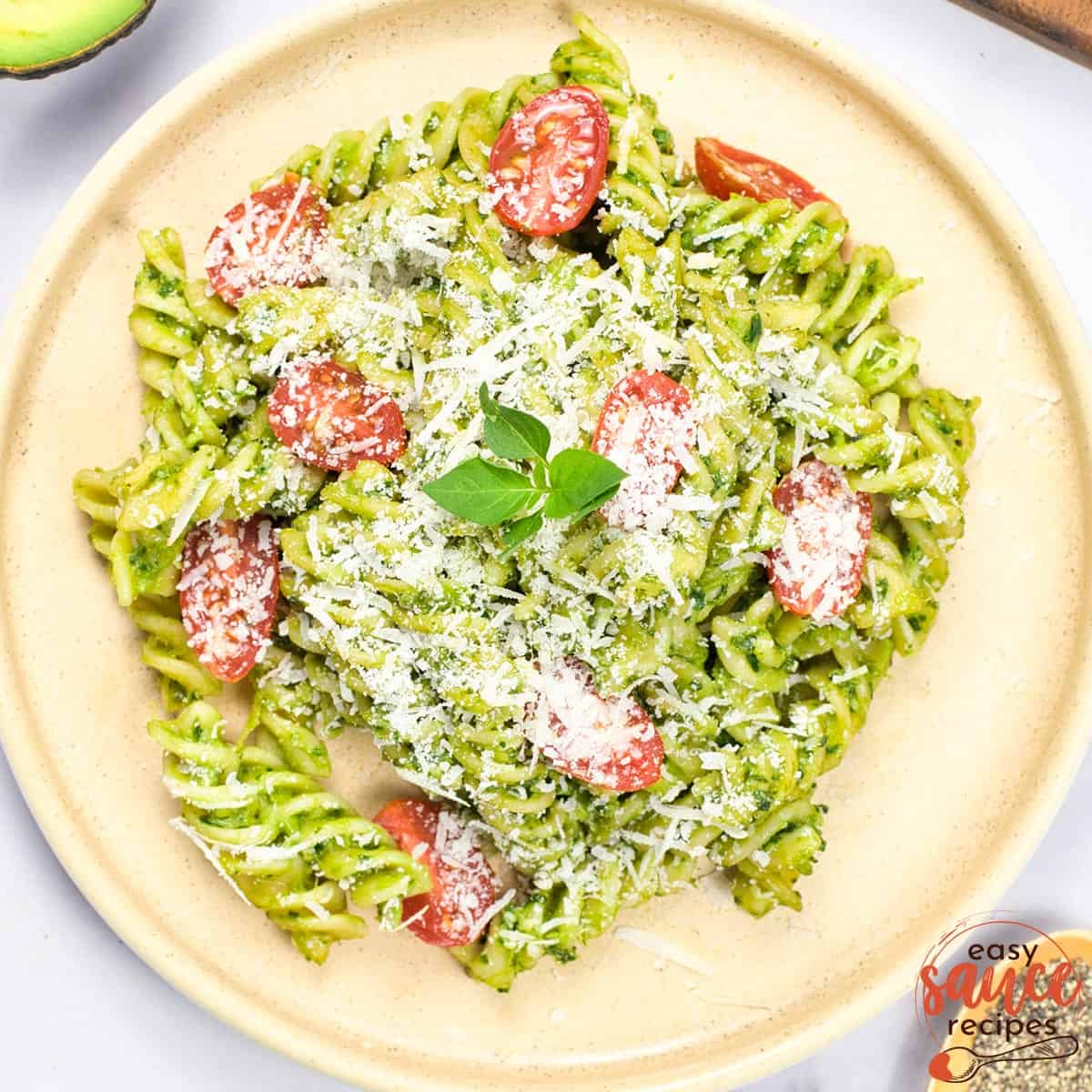 a plate full of avocado sauce pasta with cheese and tomato garnish