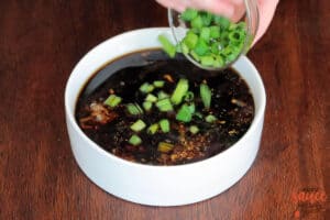 adding green onions into bulgogi sauce in a white bowl