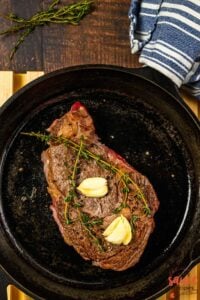 a freshly seared steak in a pan with garlic and thyme rested on top