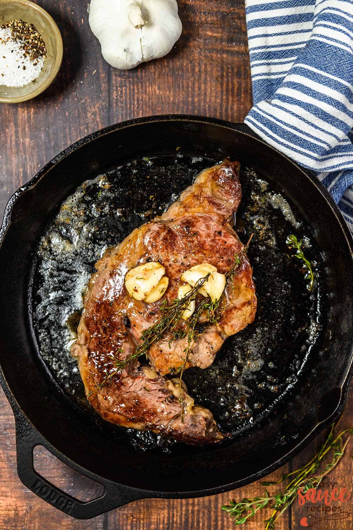 a cast iron pan with a butter basted steak, garlic, and thyme