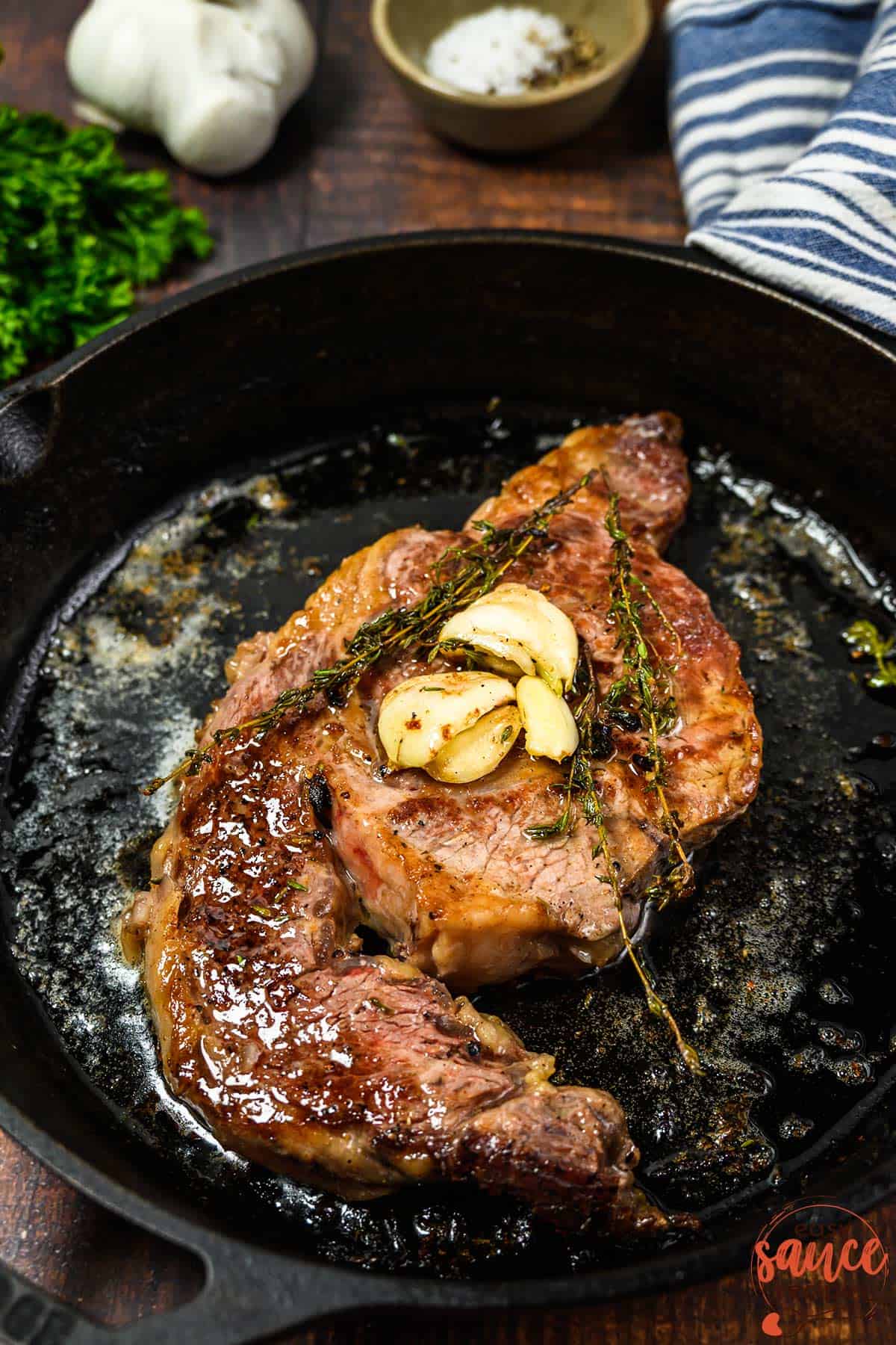 a steak in a pan to butter baste with crushed garlic and thyme