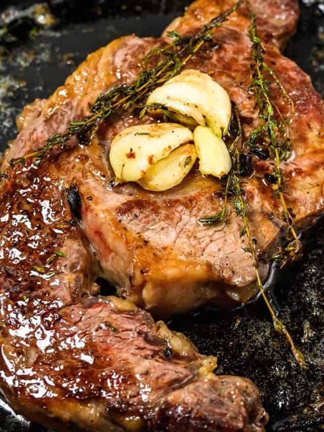 a steak basting in a cast iron pan with bubbling butter, crushed garlic, and thyme sprigs