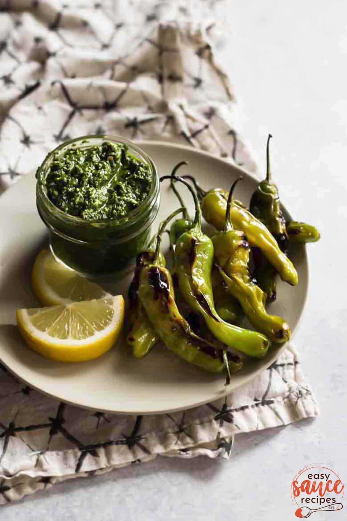 parsley pesto in a glass jar on a plate with lemon slices and blistered shishito peppers