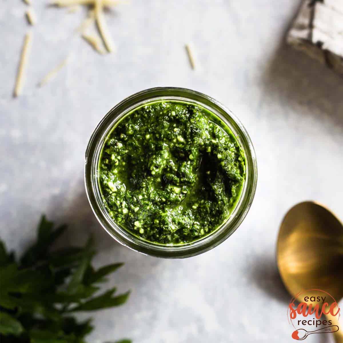 overhead of parsley pesto in a glass jar next to a spoon and additional parsley