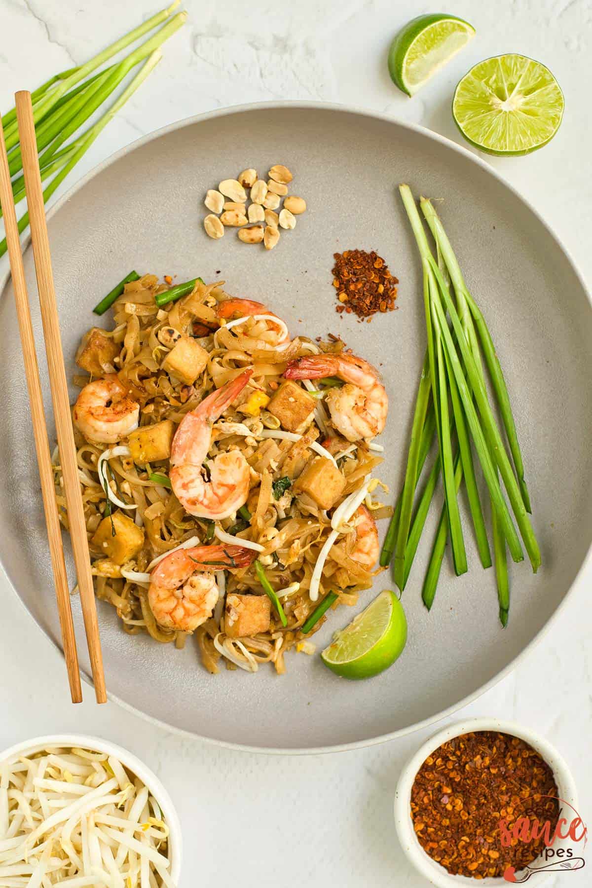 a garnished dinner plate full of completed pad thai, green onions, lime, chili, and peanuts