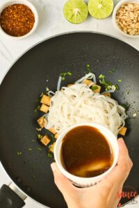 mixed pad thai sauce in a dish held over a pan of cooked noodles and tofu