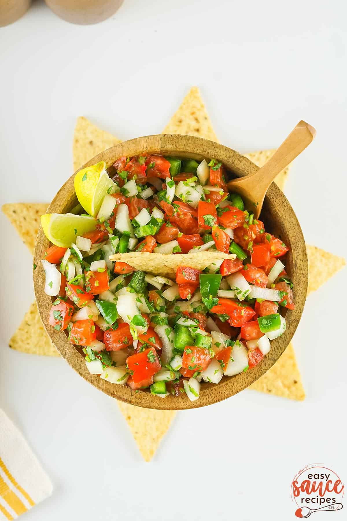 pico de gallo in a brown bowl with tortilla chips surrounding the bowl