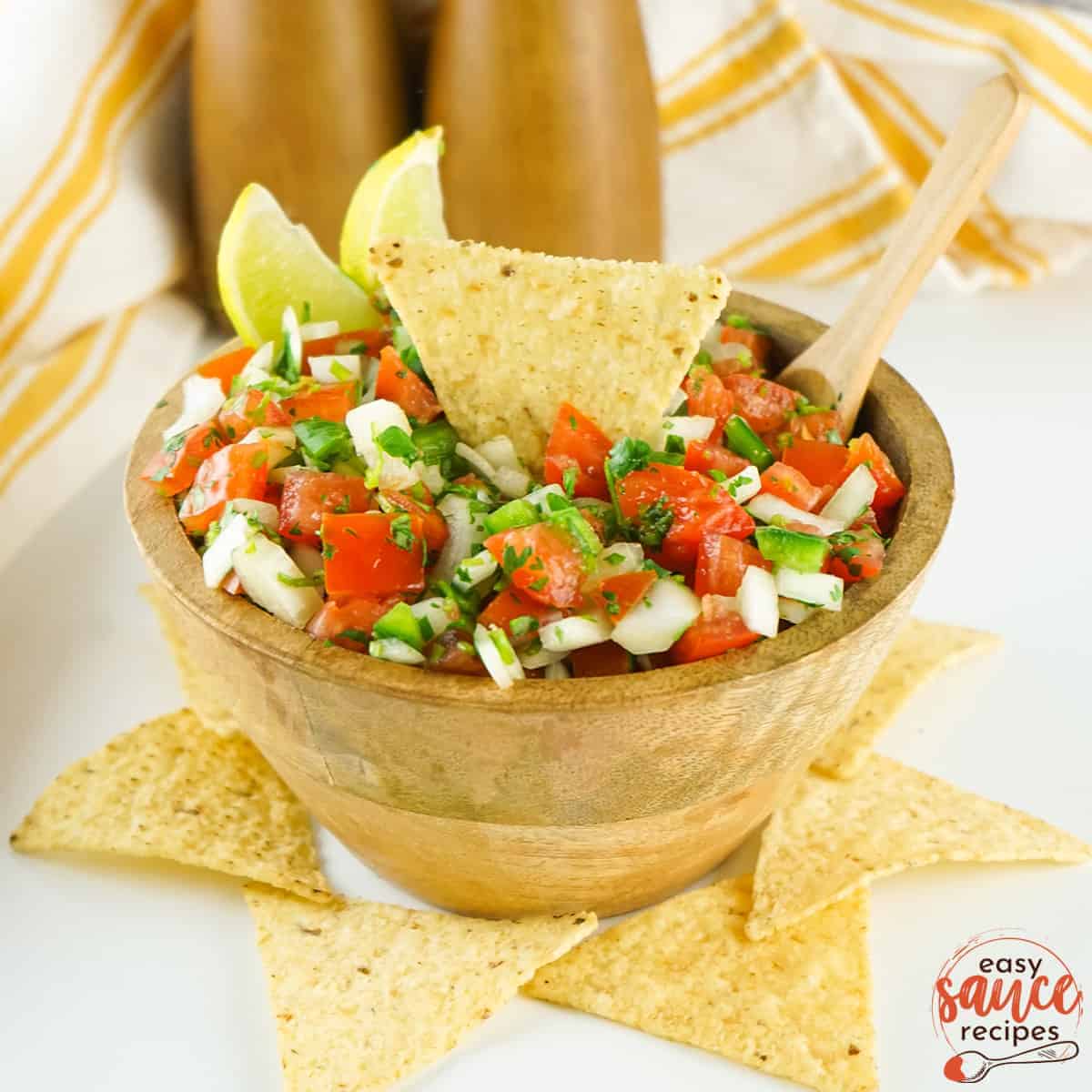 pico de gallo in a brown bowl with tortillas chips and slices of limes