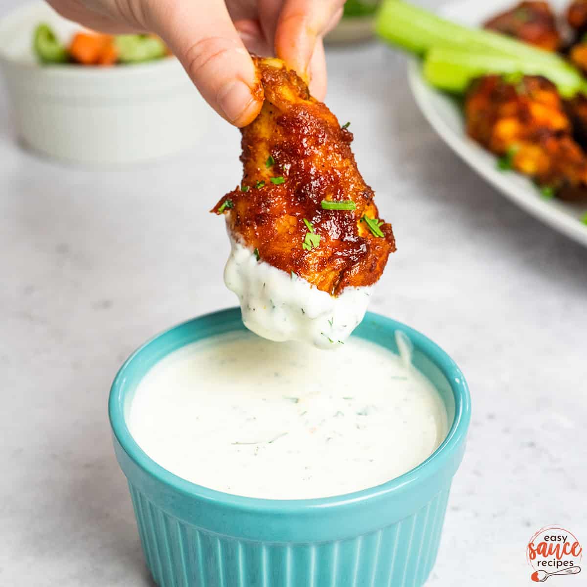 ranch in a blue dish with a wing over top