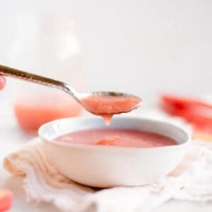 a spoon dripping rhubarb sauce over a white bowl