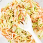 mixed coleslaw and dressing in a bowl with a white spoon