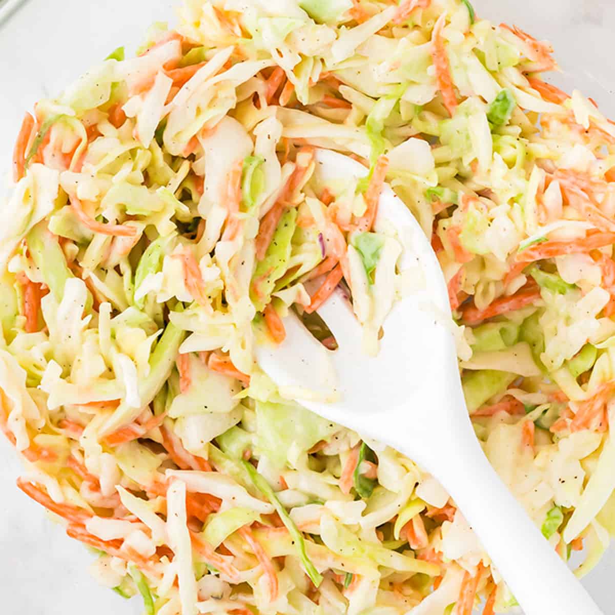 mixed coleslaw and dressing in a bowl with a white spoon