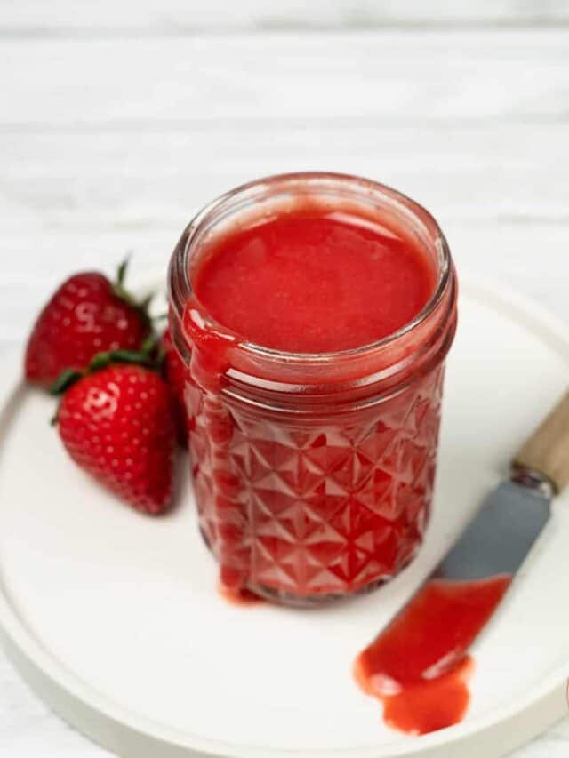 strawberry sauce in a clear mason jar with a butter knife and fresh strawberries on the side