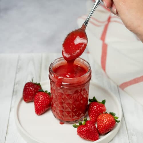 a spoon dripping strawberry sauce into a clear mason jar