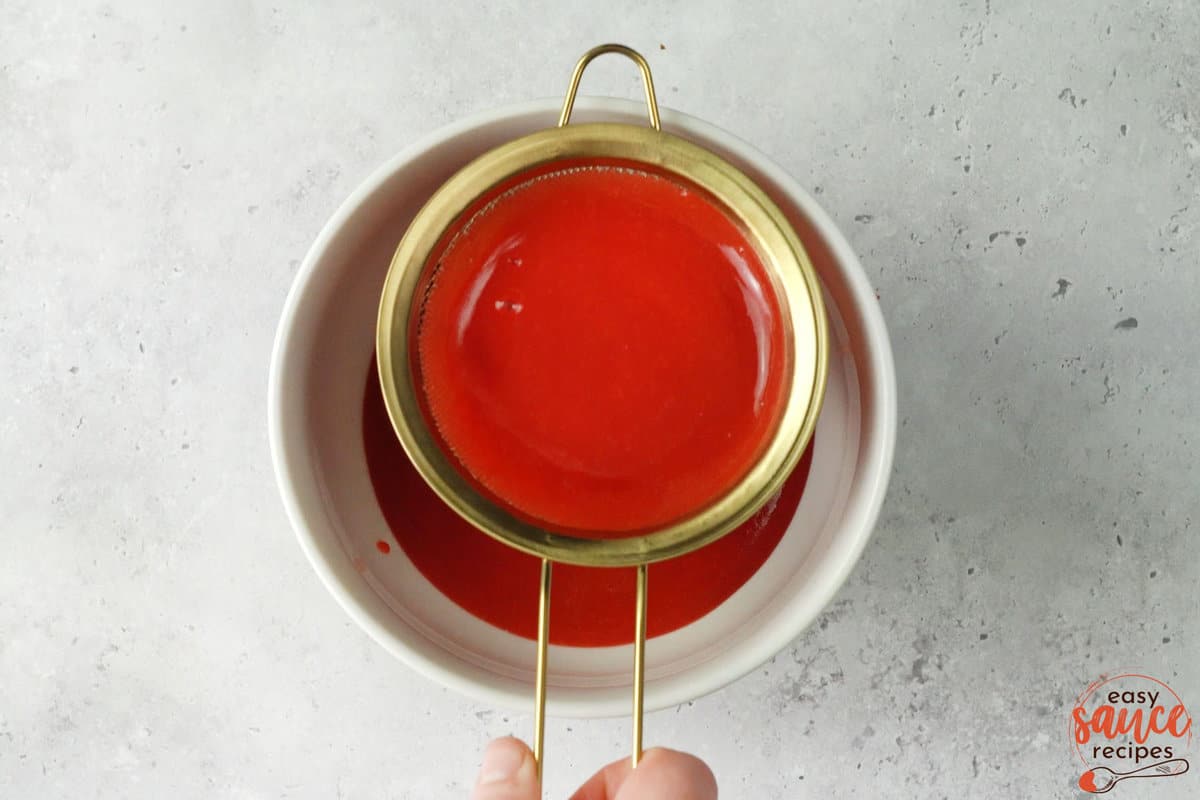 straining strawberry sauce into a bowl