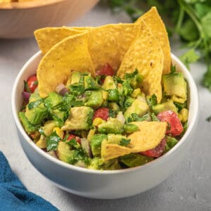 avocado salsa in a white bowl with chips dipped in
