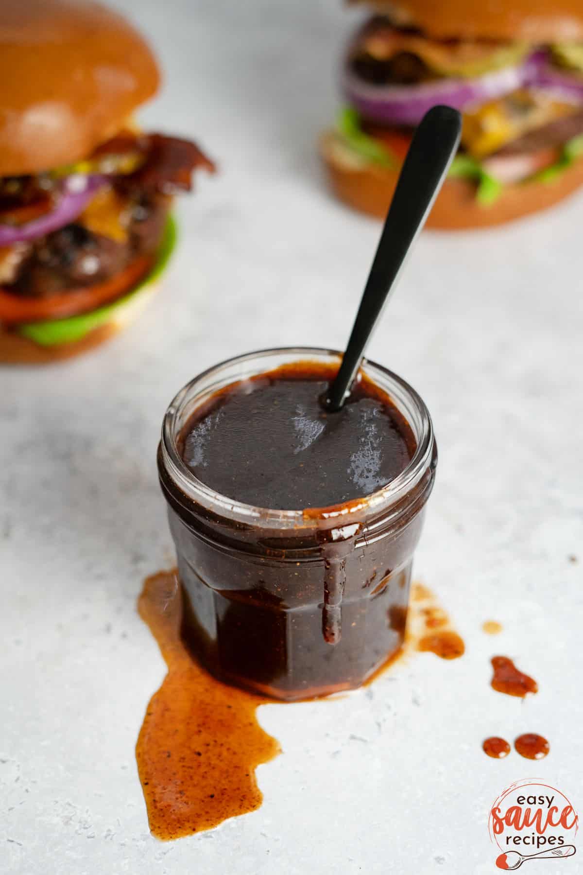 bbq sauce in a clear jar with a spoon inside of the jar