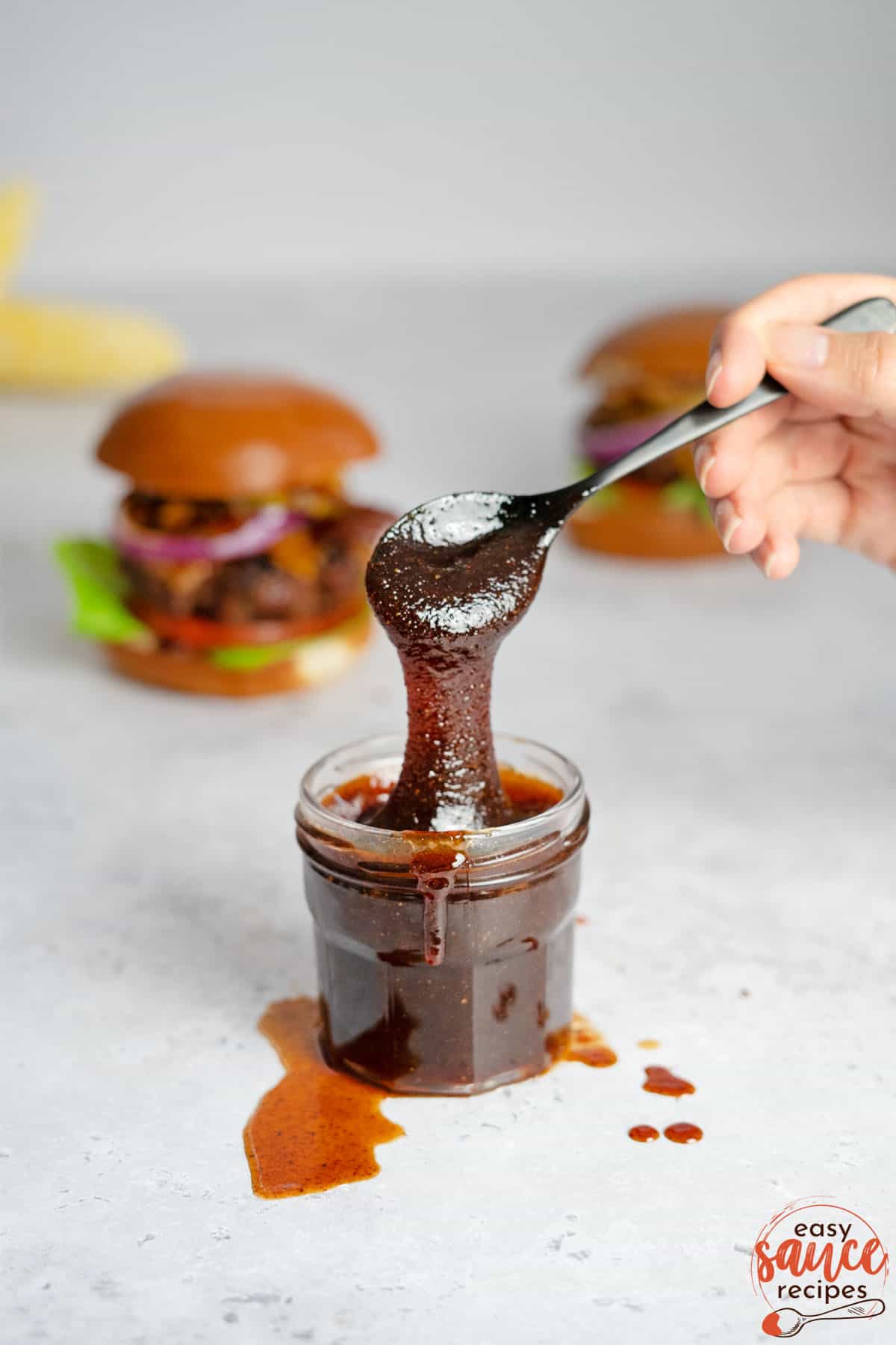 bbq sauce in a clear jar with a spoon pouring sauce
