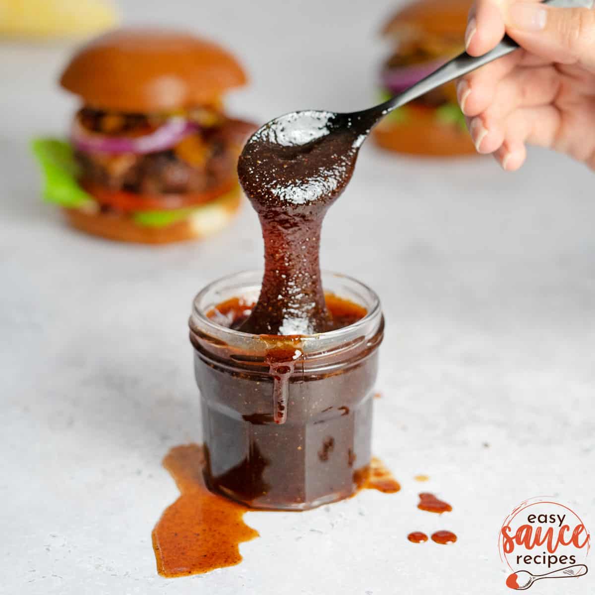bbq sauce in a clear jar with a spoon dripping sauce down