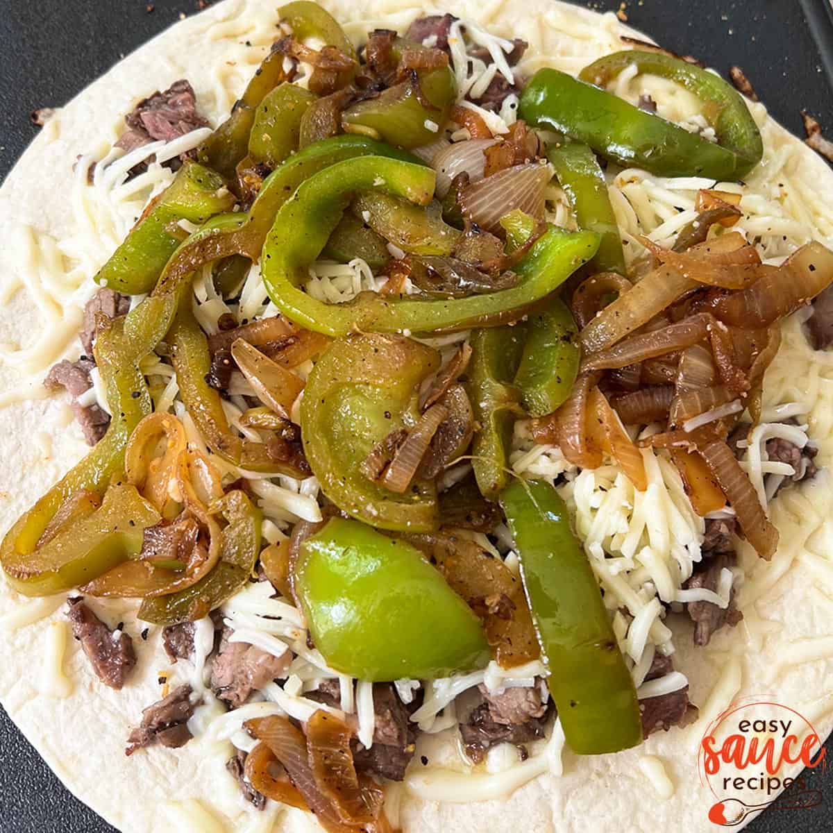 a fajita with peppers and onions on top of cheese and steak