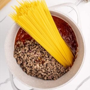 adding spaghetti pasta to a pot with beef and sauce