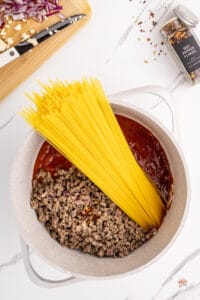 spaghetti pasta added to a pot with sauce and meat