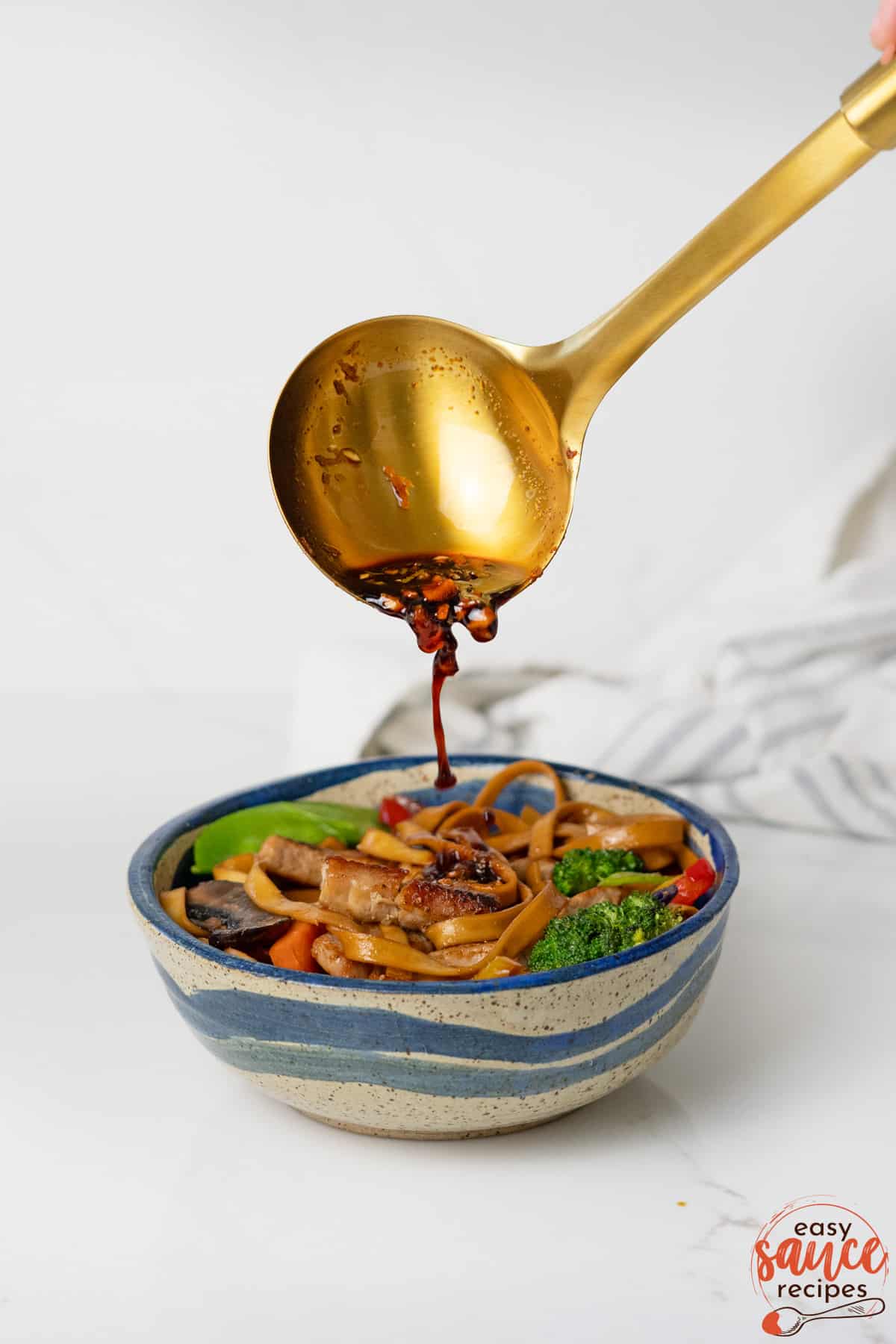 teriyaki sauce in a gold spoon pouring over bowl of food