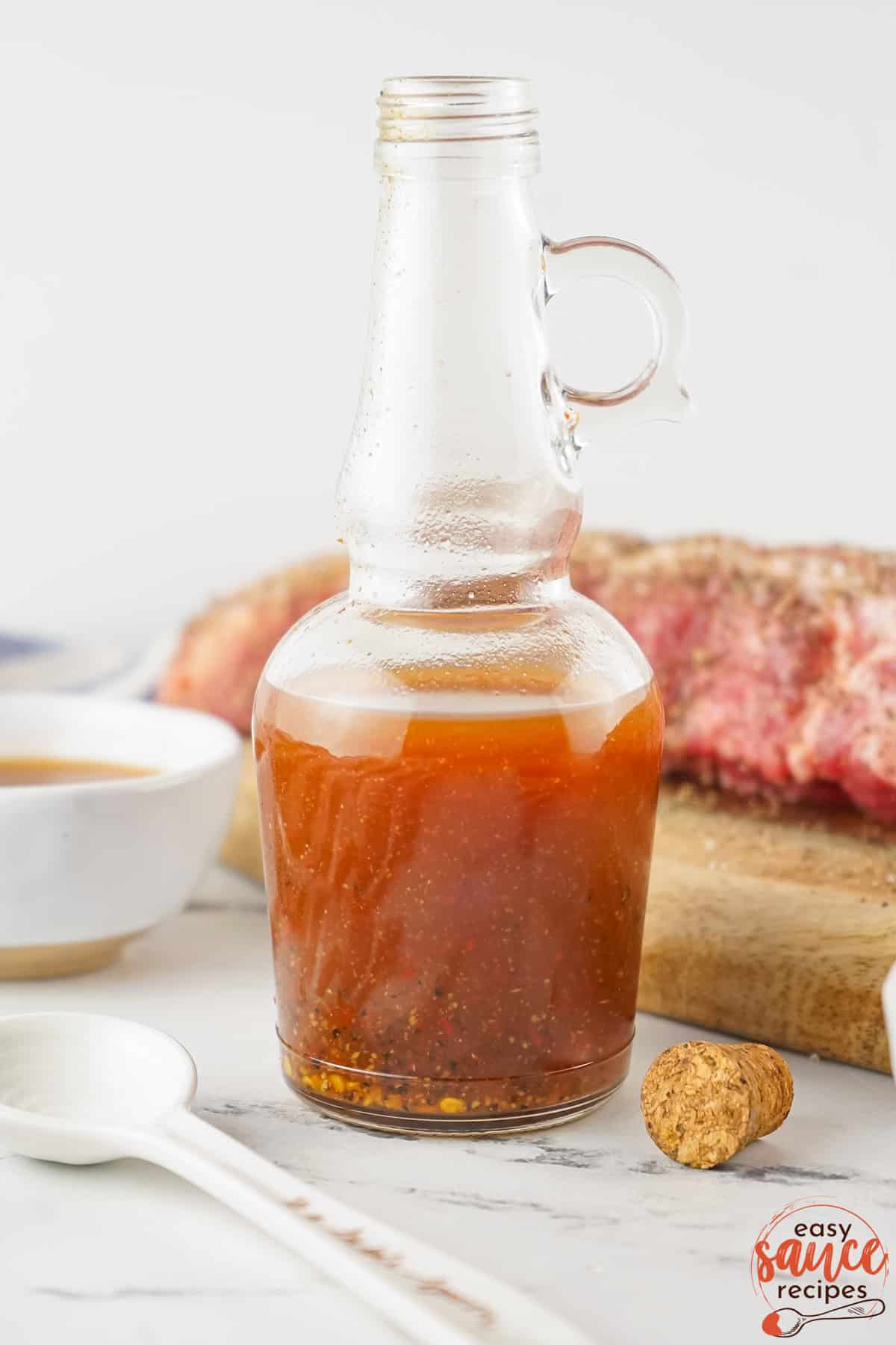 a half-filled bottle of vinegar BBQ sauce with ribs in the background