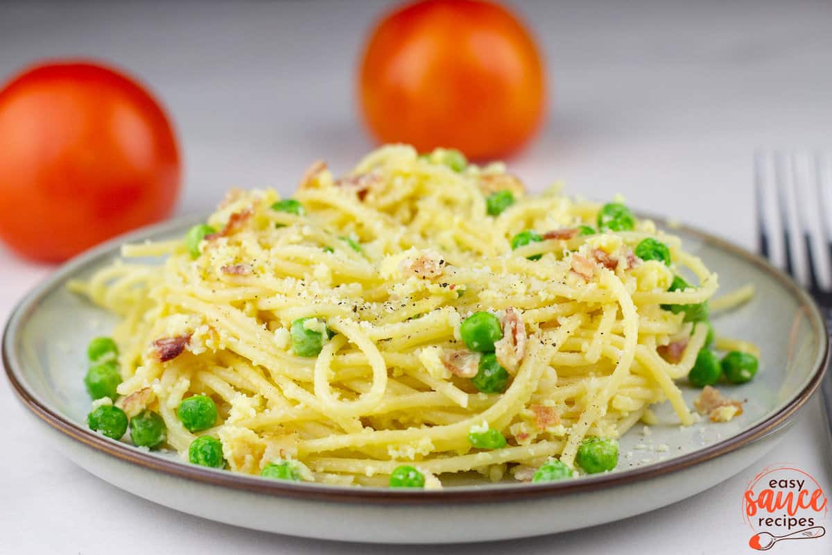 carbonara sauce on pasta on a plate with tomatoes in the background